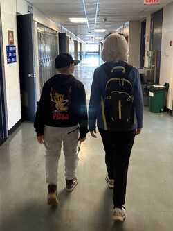 Student uses a long cane as he walks beside his O&amp;M specialist. 