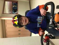 Student wears a helmet and has both hands on the handlebars of an adapted bicycle