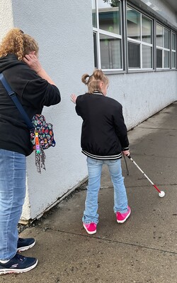 Intervenor watches as her student walks with her left hand in a modified upper protective position while she sweeps her cane