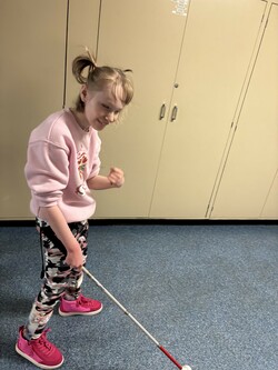 Student looks toward the camera with a big smile on her face as she holds her long cane. 