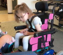 Student in a wheelchair looks closely at the AFO to determine which foot to put in. 